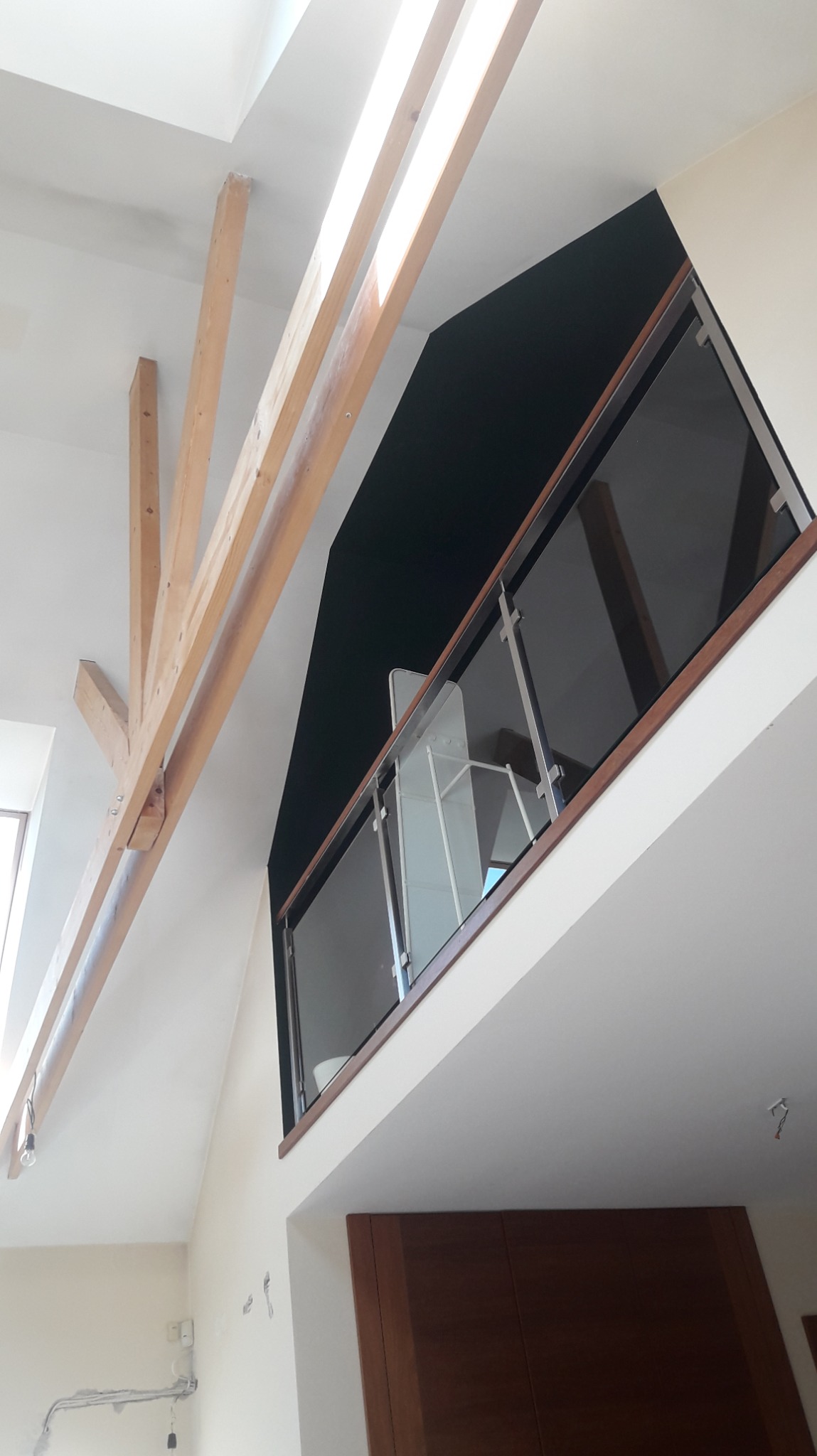 Nowoczesne wykończenie wnętrza z drewnianą konstrukcją stropu i szklaną balustradą na antresoli. Widok z dołu, jasne ściany, minimalistyczny design.