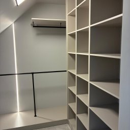 Lordom Sp z o.o. - Półki wnękowe z oświetleniem LED w garderobie na poddaszu. Czarny drążek na ubrania. Minimalistyczny design, jasne kolory, nowoczesne wykończenie.