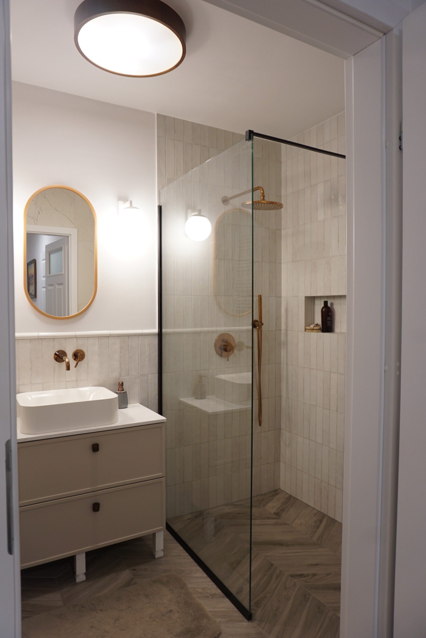 Wykończona łazienka w odcieniach bieli i beżu z kabiną prysznicową ze złotymi akcentami, umywalką nablatową i lustrem w złotej ramie. Parkiet ułożony w jodełkę.