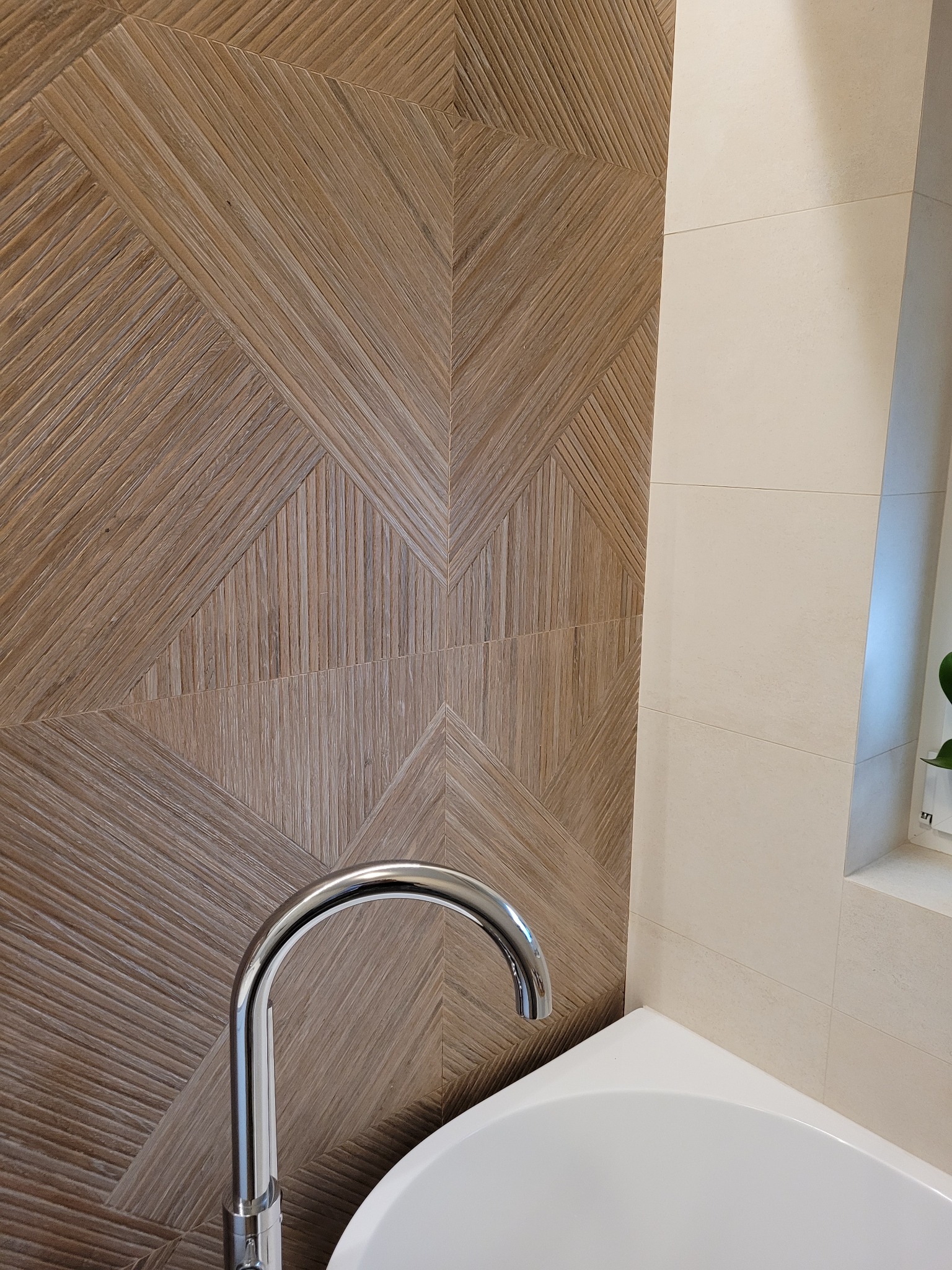 Wnętrze łazienki z drewnopodobną okładziną ścienną ułożoną w geometryczny wzór. Widoczna bateria umywalkowa i fragment białej wanny.