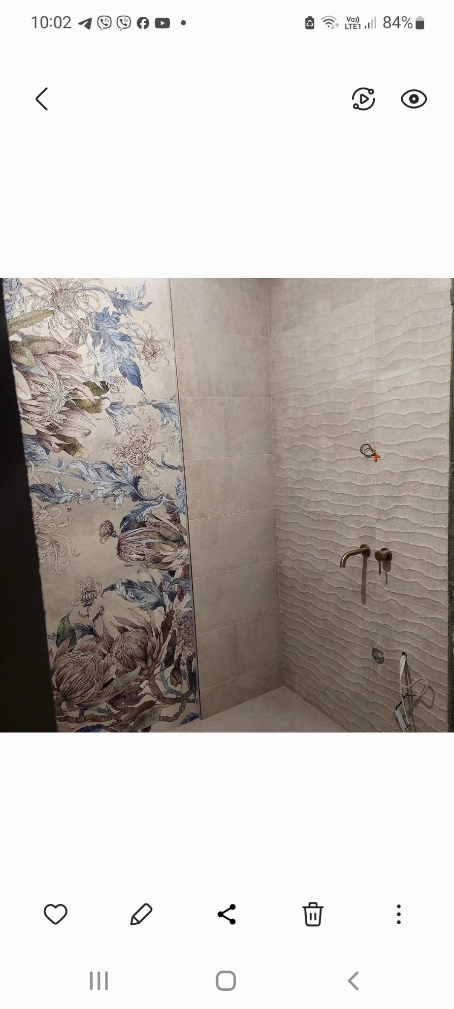 Wykończona łazienka z płytkami: po lewej stronie płytki z motywem kwiatowym, po prawej płytki beżowe z fakturą fal, armatura w kolorze starego złota.