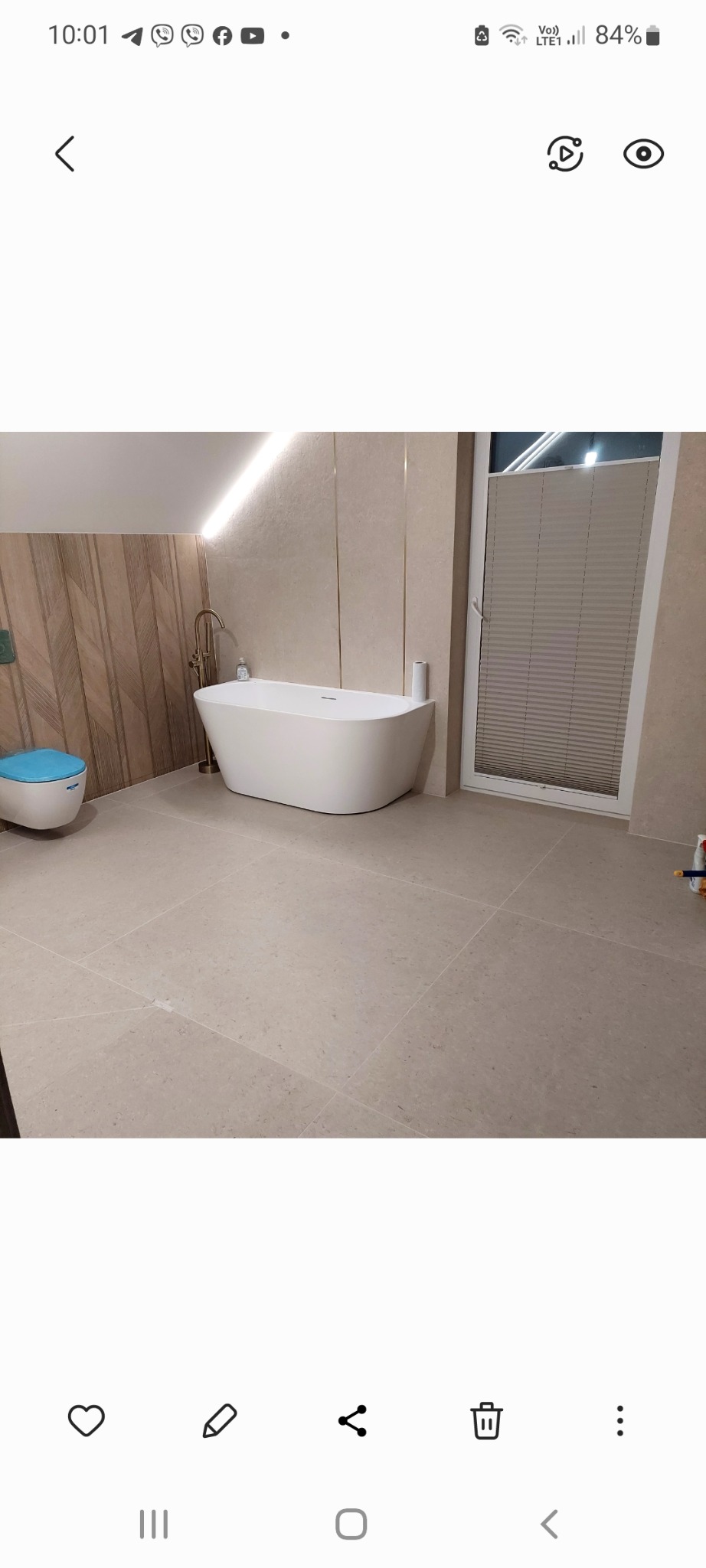 Nowoczesna łazienka z wolnostojącą białą wanną, podświetleniem LED, beżowymi płytkami podłogowymi i ściennymi oraz toaletą w kolorze błękitnym.