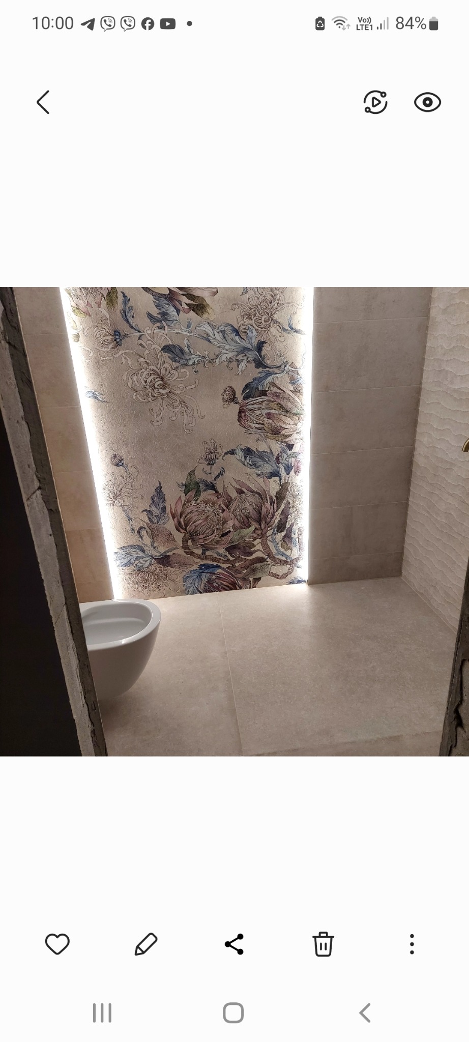 Nowoczesna łazienka z beżowymi płytkami, ścianą akcentową z motywem kwiatowym podświetloną LED, i wiszącą toaletą.