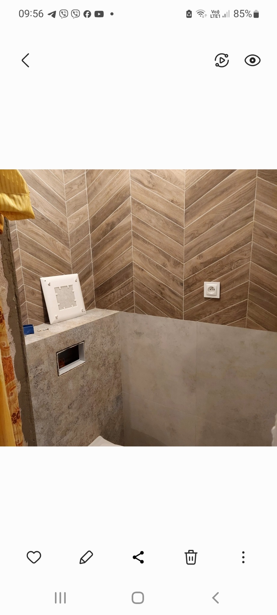 Montaż płytek imitujących drewno w jodełkę na ścianie, z widocznym otworem na stelaż podtynkowy WC i gniazdkiem elektrycznym, w trakcie prac wykończeniowych.