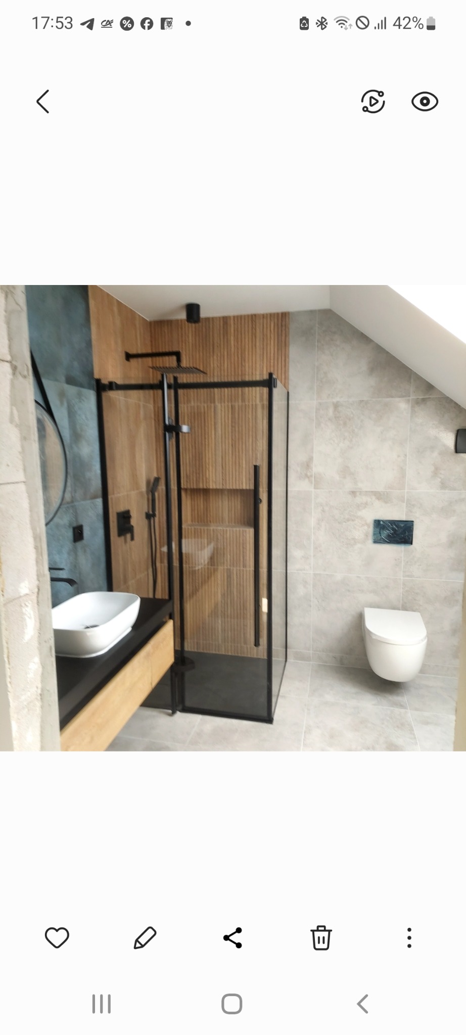 Nowoczesna łazienka na poddaszu z kabiną prysznicową typu walk-in z czarnymi ramami, umywalką nablatową i podwieszaną toaletą. Ściany wyłożone płytkami w odcieniach szarości i drewna.