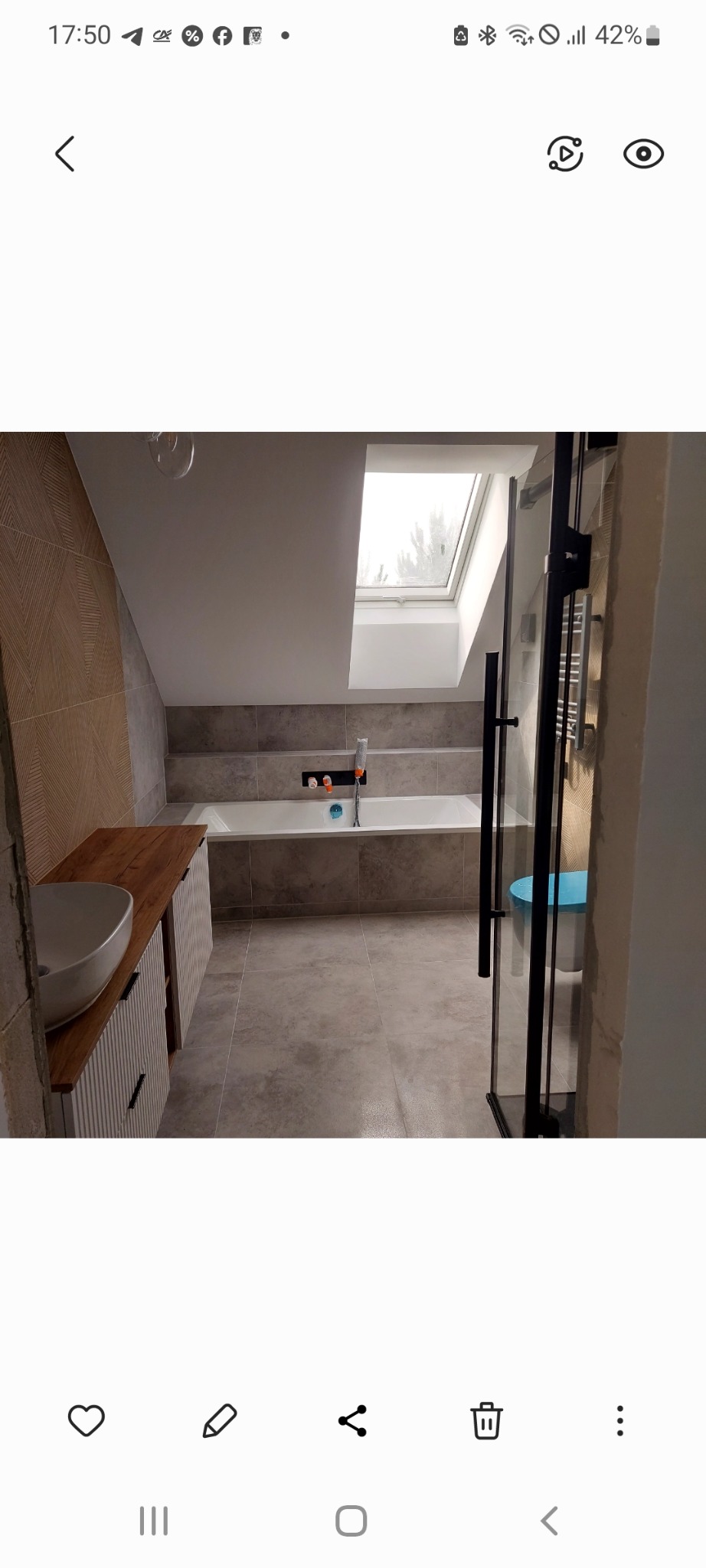 Wykończona łazienka na poddaszu z wanną, umywalką nablatową i kabiną prysznicową. Uwagę zwracają płytki imitujące drewno na ścianie i okno dachowe.