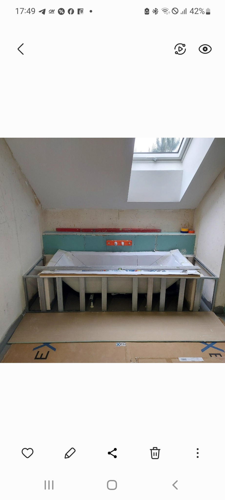 Wnęka z wanną w trakcie obudowy płytami gipsowo-kartonowymi. Widoczne profile metalowe, poziomica i fragment okna dachowego. Prace wykończeniowe w łazience.