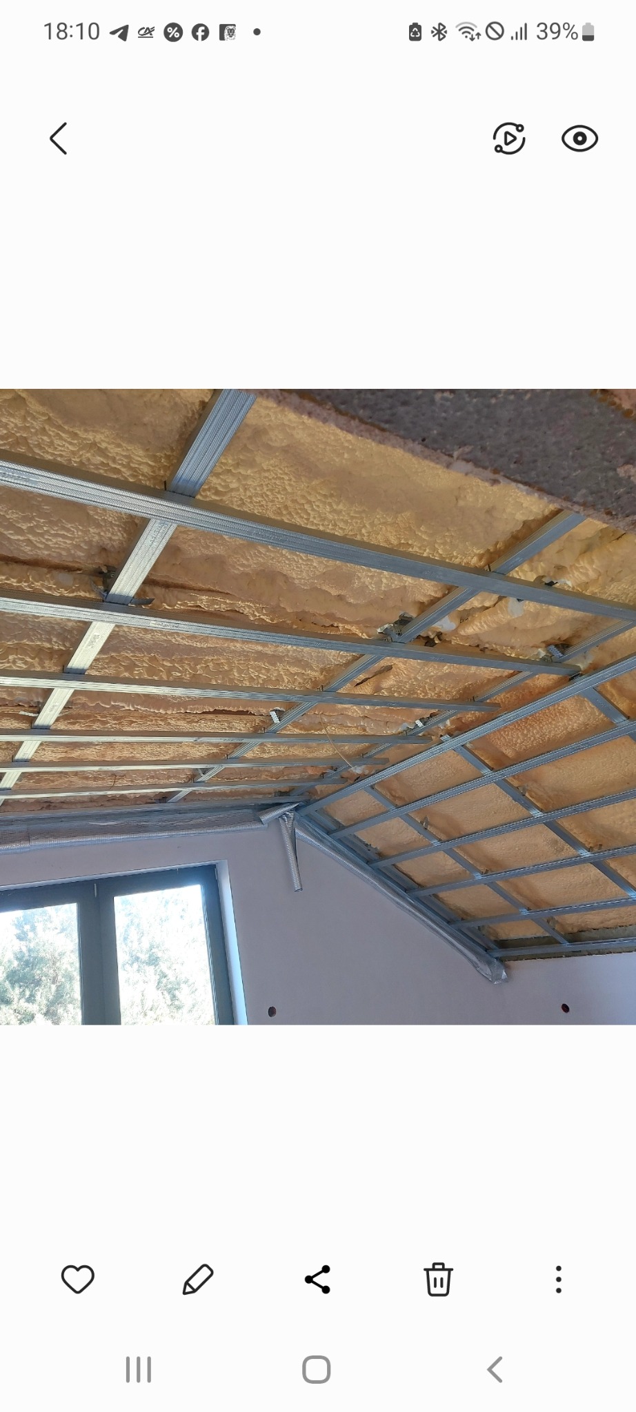 Widok na sufit z zamontowaną metalową konstrukcją pod płyty. W przestrzeniach beżowa wełna mineralna. Fragment okna w lewym dolnym rogu.