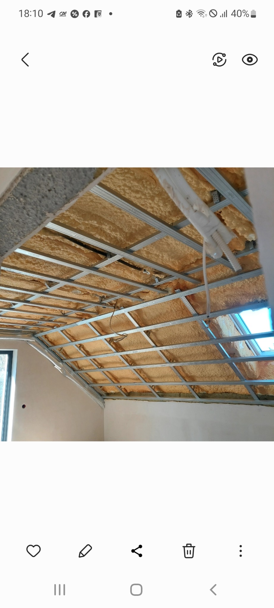 Sufit podwieszany z metalową konstrukcją i izolacją z pianki, widok z dołu. Fragment okna w tle. Etap prac wykończeniowych w jasnym pomieszczeniu.