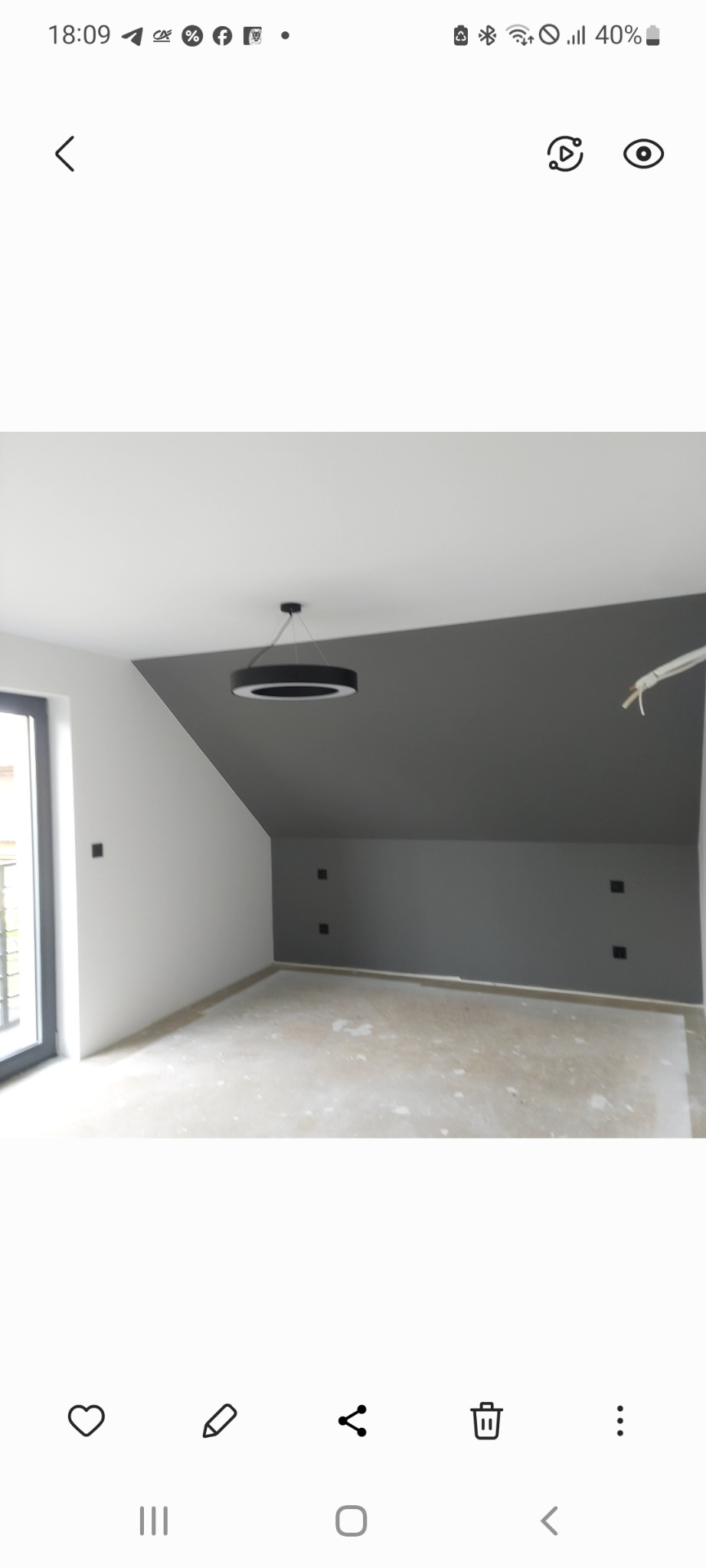 Pomieszczenie po remoncie z szarą ścianą ze skosem, białymi ścianami bocznymi i nowoczesną lampą sufitową. Widoczne gniazdka elektryczne.