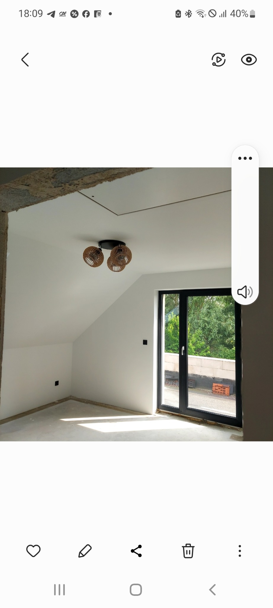 Poddasze po remoncie: białe ściany, okno balkonowe z czarną ramą, nowoczesna lampa sufitowa. Część ściany z surowym wykończeniem. Jasne wnętrze z widokiem na zieleń.