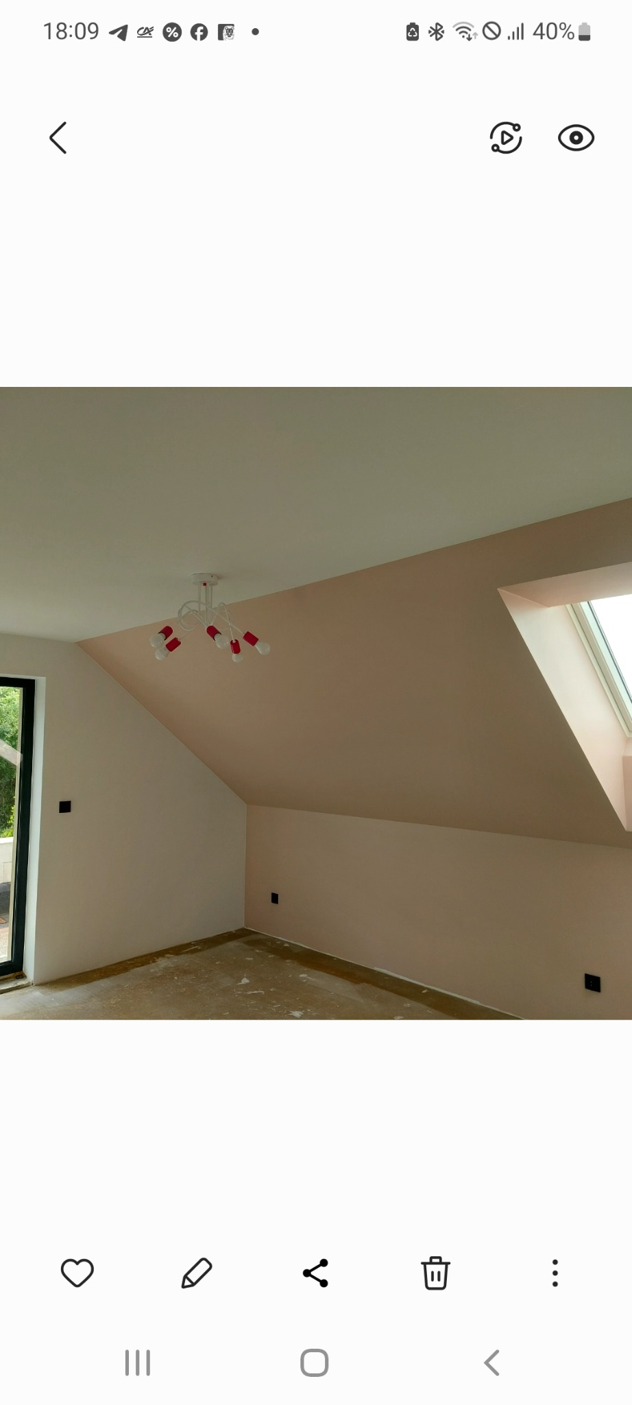 Pokój na poddaszu po malowaniu ścian na jasny róż, z oknem dachowym i nowoczesną lampą z czerwonymi detalami. Podłoga przygotowana do dalszych prac.