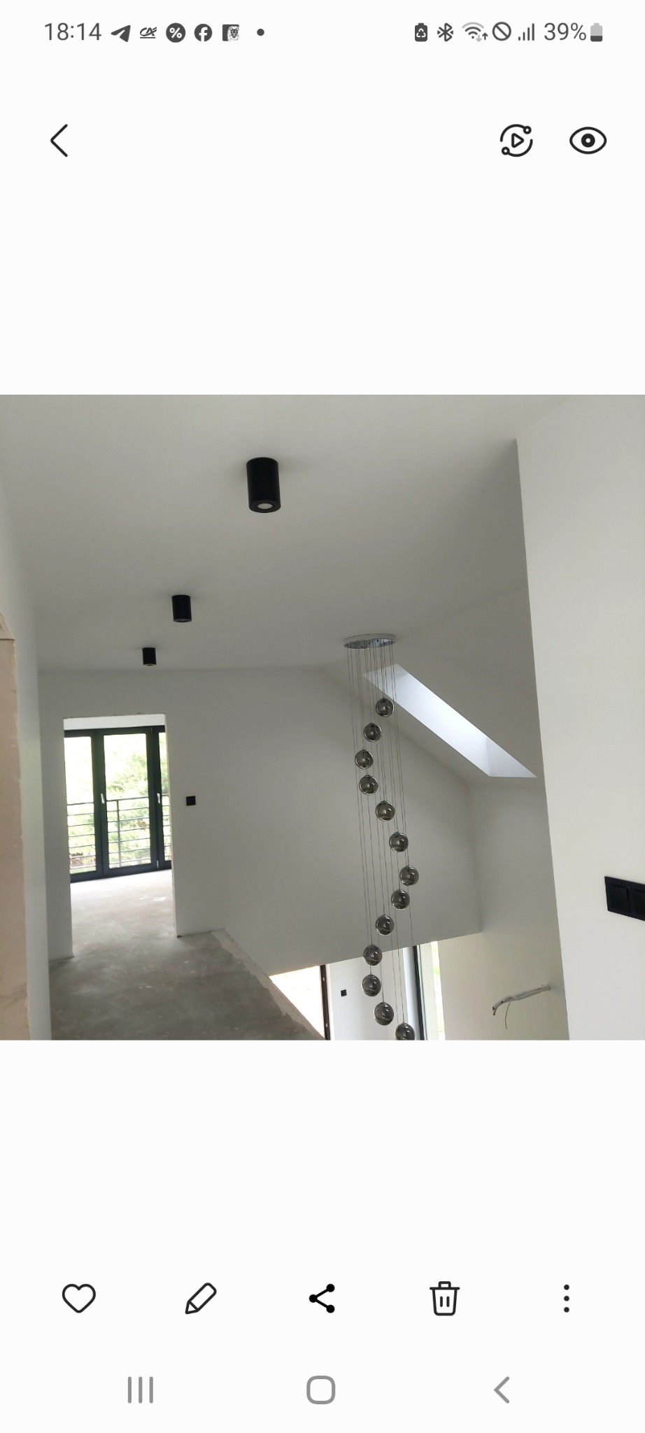 Wnętrze domu w stanie deweloperskim: surowe ściany, widoczne instalacje elektryczne, minimalistyczne oświetlenie sufitowe i zwisająca lampa kulista.