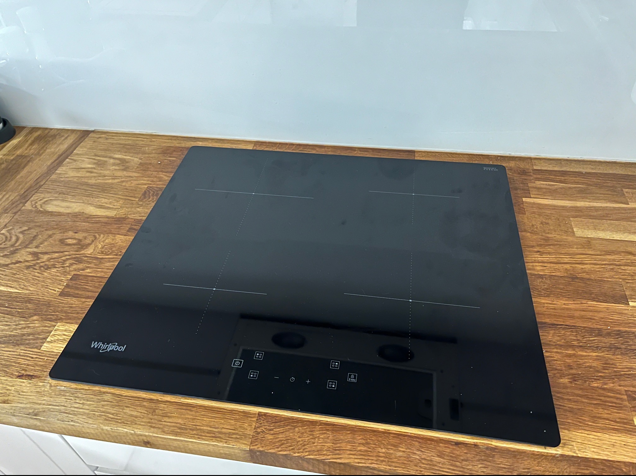 Czarna płyta indukcyjna Whirlpool zamontowana w drewnianym blacie kuchennym, widoczne oznaczenia pól grzewczych i panel sterowania dotykowego.