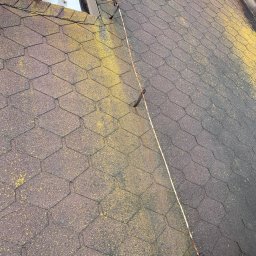 MatGras - Brązowy dach pokryty bitumiczną dachówką z wyraźnym żółtym nalotem mchu po lewej stronie i systemem odgromowym biegnącym wzdłuż krawędzi.