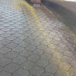 MatGras - Dach pokryty bitumiczną dachówką, widoczne zabrudzenia i porosty, ceglany komin w tle.