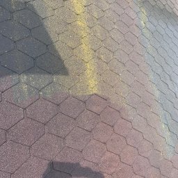 MatGras - Dach pokryty gontem bitumicznym w kształcie plastra miodu, częściowo pokryty żółtym pyłem, z widocznym cieniem osoby robiącej zdjęcie.