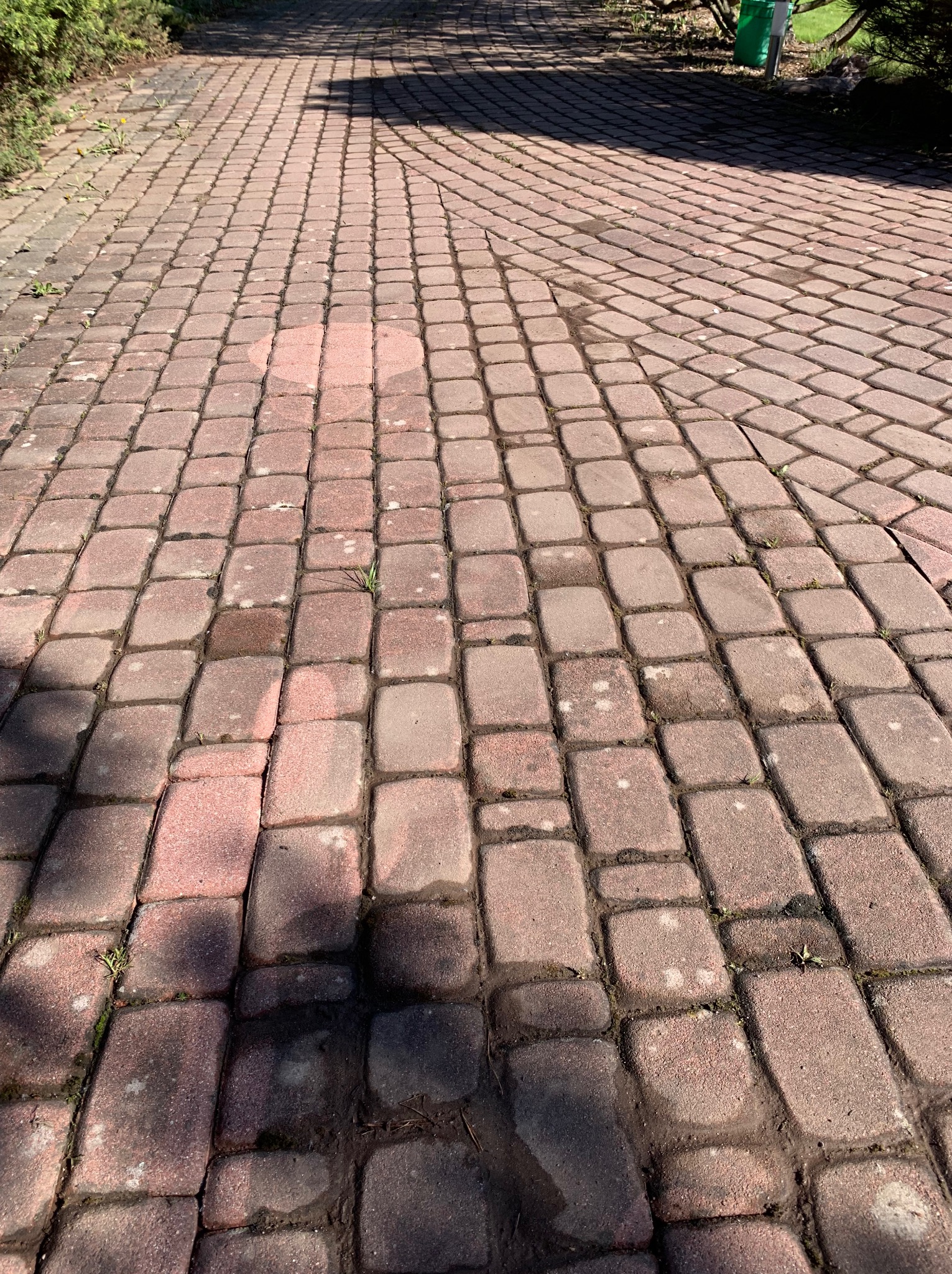 Czerwona kostka brukowa z widocznymi śladami zabrudzeń i zacienieniami, sugerująca potrzebę czyszczenia. Widoczne drobne rośliny w szczelinach.