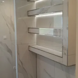 Nowoczesna łazienka z marmurowymi płytkami, podświetlanymi półkami i szarą podłogą.