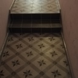 Valdibud - Korytarz z nową, wzorzystą podłogą z płytek i schodami wykończonymi ciemnymi płytkami.