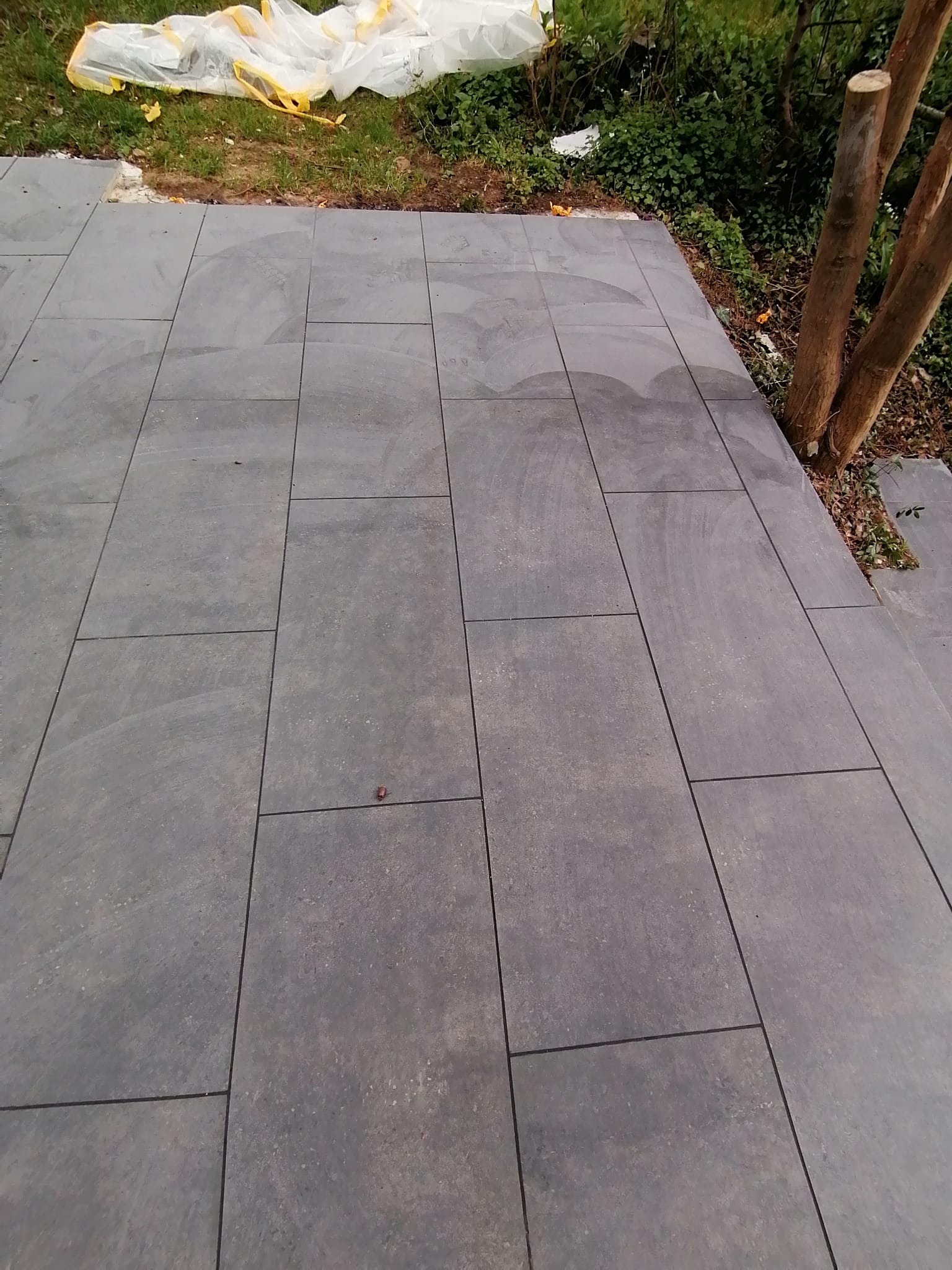 Świeżo ułożona, szara, prostokątna kostka brukowa na zewnątrz, z widocznymi śladami po budowie i przykrytą folią częścią terenu obok.