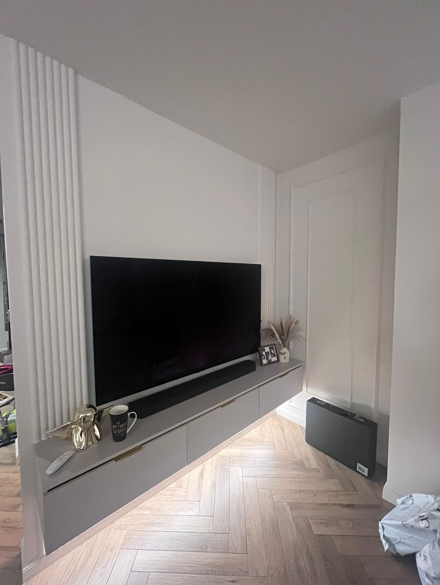 Nowoczesny salon z telewizorem na szafce RTV, dekoracyjne listwy ścienne i parkiet w jodełkę. Minimalistyczne wykończenie wnętrza.