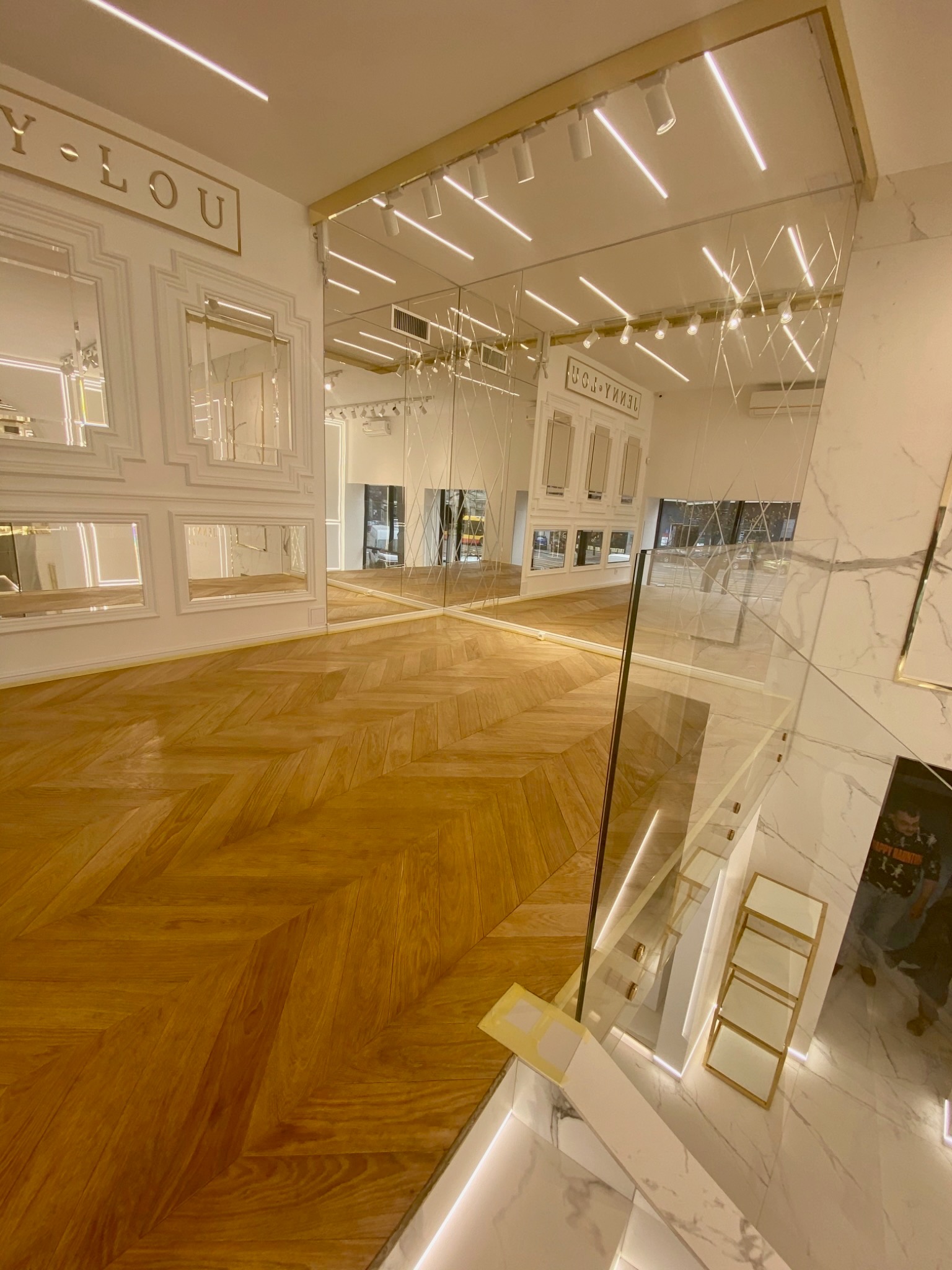 Eleganckie wykończenie wnętrza sklepu: parkiet w jodełkę, lustra w ozdobnych ramach, marmurowe ściany i oświetlenie LED. Widok z góry na schody.