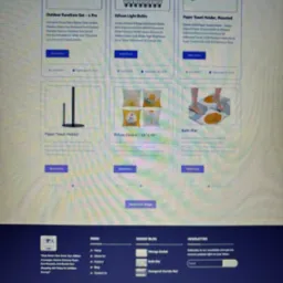 Fragment strony internetowej sklepu z artykułami wyposażenia domu, prezentujący ofertę mebli ogrodowych, żarówek Edison, uchwytów na ręczniki papierowe, poszewek na poduszki i mat łazienkowych.