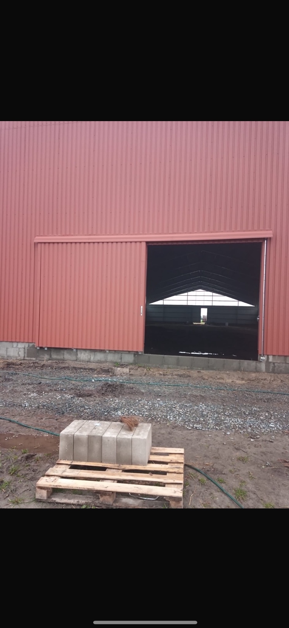 Budowa hali z płyt warstwowych: widok na otwartą halę z częściowo odsuniętymi drzwiami przesuwnymi, na pierwszym planie paleta z bloczkami betonowymi.