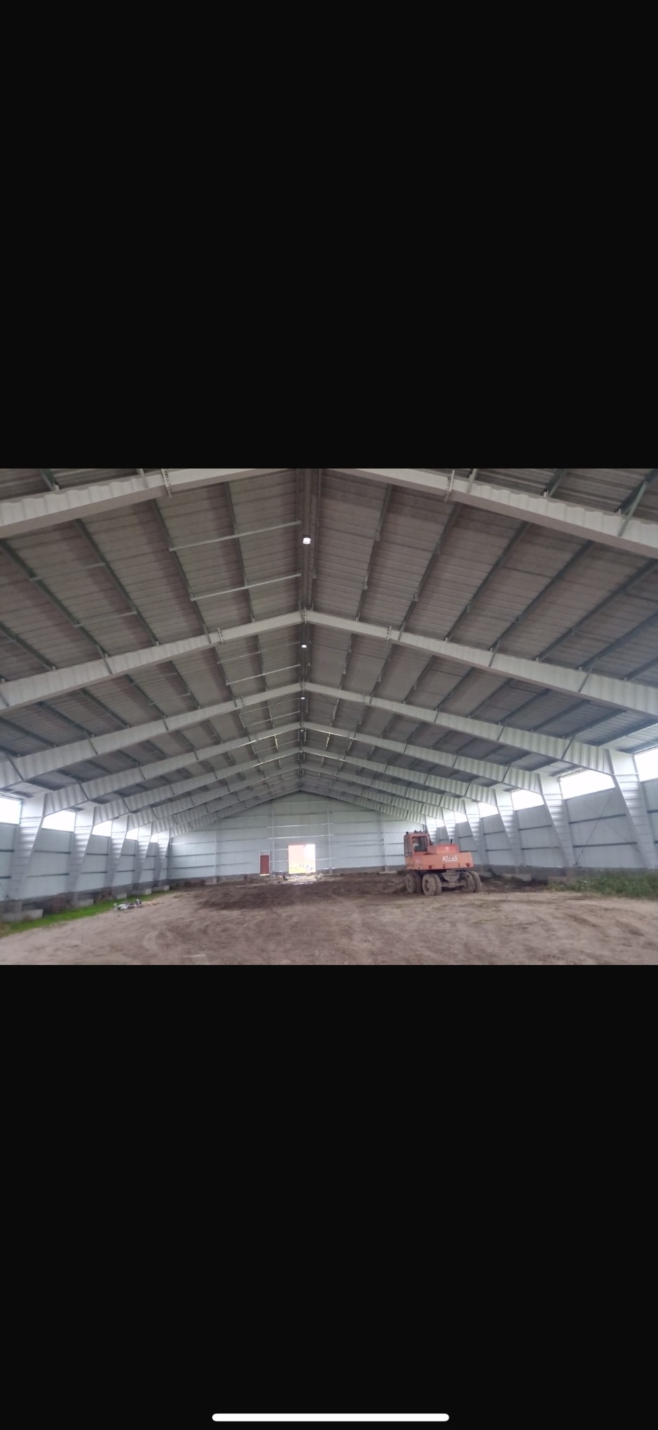 Wnętrze nowo wybudowanej hali stalowej z jasnymi panelami ściennymi i dachem, widoczny sprzęt budowlany w środku, ziemia wewnątrz hali przygotowana do dalszych prac.