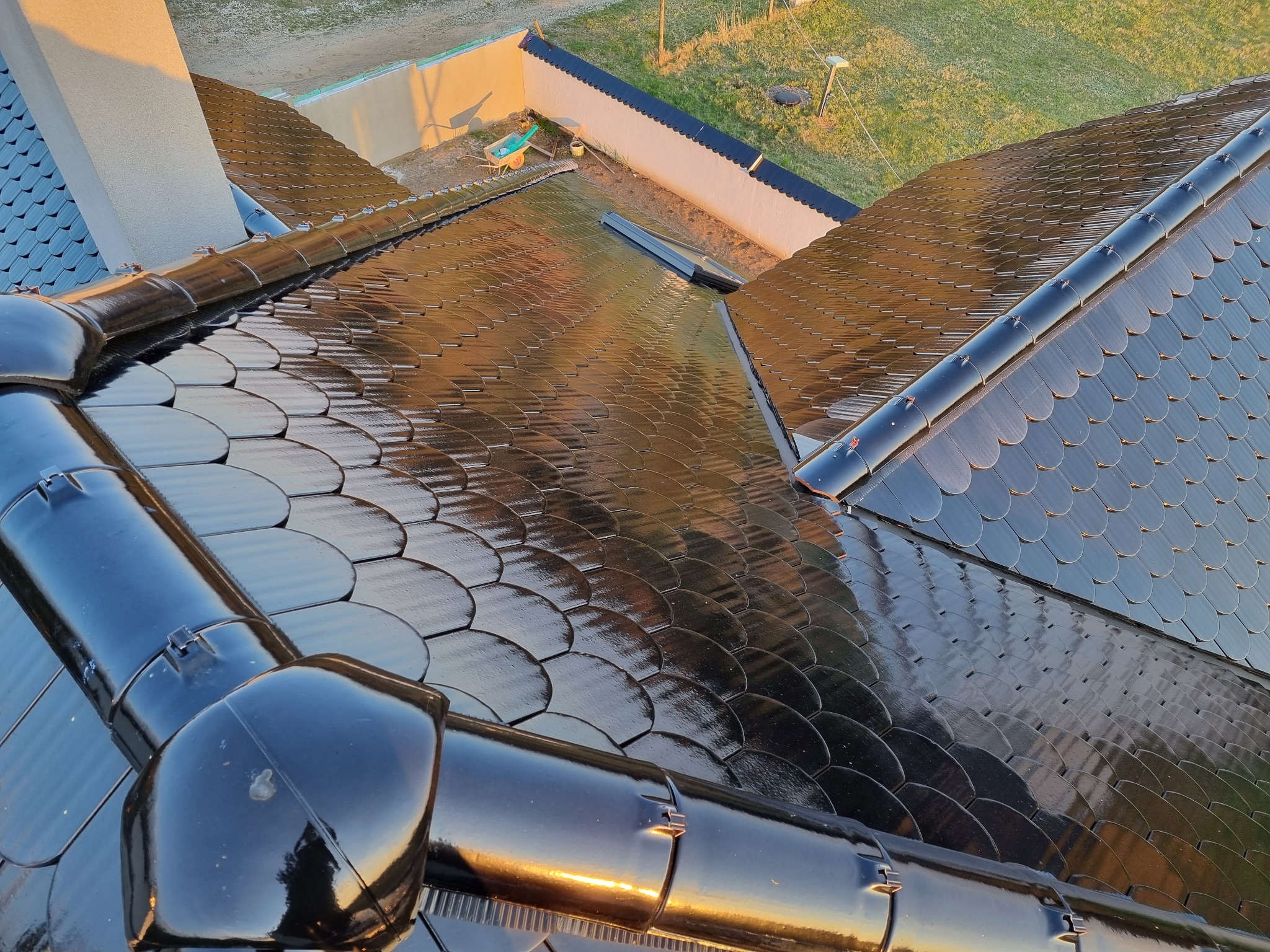 Błyszczący dach pokryty czarną dachówką karpiówką, widok z góry na nowo wykończony dach domu w słoneczny dzień.