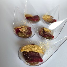 TASTY CATERING Tomasz Szmidt - Eleganckie finger food: pięć przezroczystych łyżeczek z ciemną pastą, burakiem i kruchym ciastkiem posypanym złotym pyłem, ułożone na białym tle.