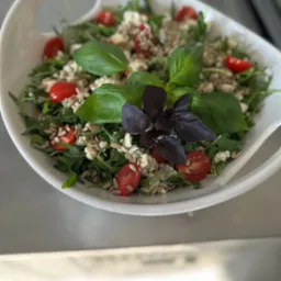 Świeża sałatka z rukoli, pomidorków cherry, sera pleśniowego i prażonych ziaren słonecznika, udekorowana świeżą bazylią w białej misce.