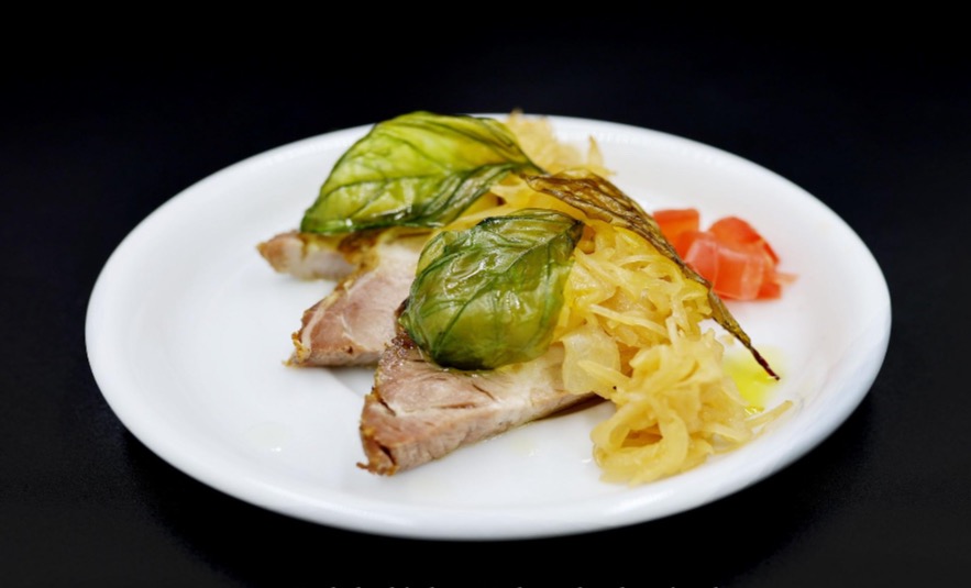 Delikatnie przypieczone plastry mięsa z kapustą, pomidorami i listkami bazylii na białym talerzu, usługa cateringowa w Markach.