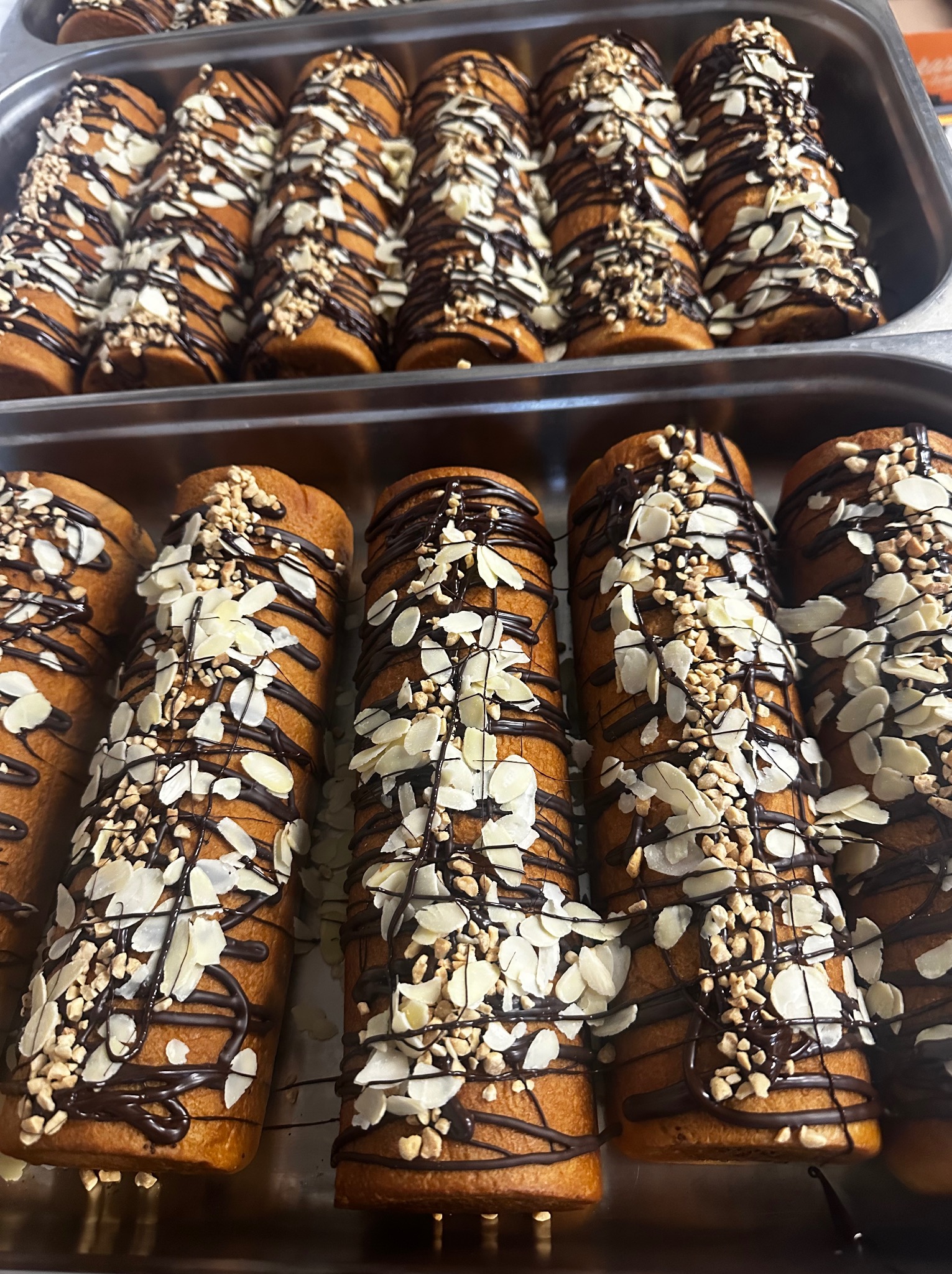 Ręcznie dekorowane babeczki w metalowej formie, polane czekoladą i posypane płatkami migdałów oraz orzechami, gotowe do serwowania na przyjęciu.