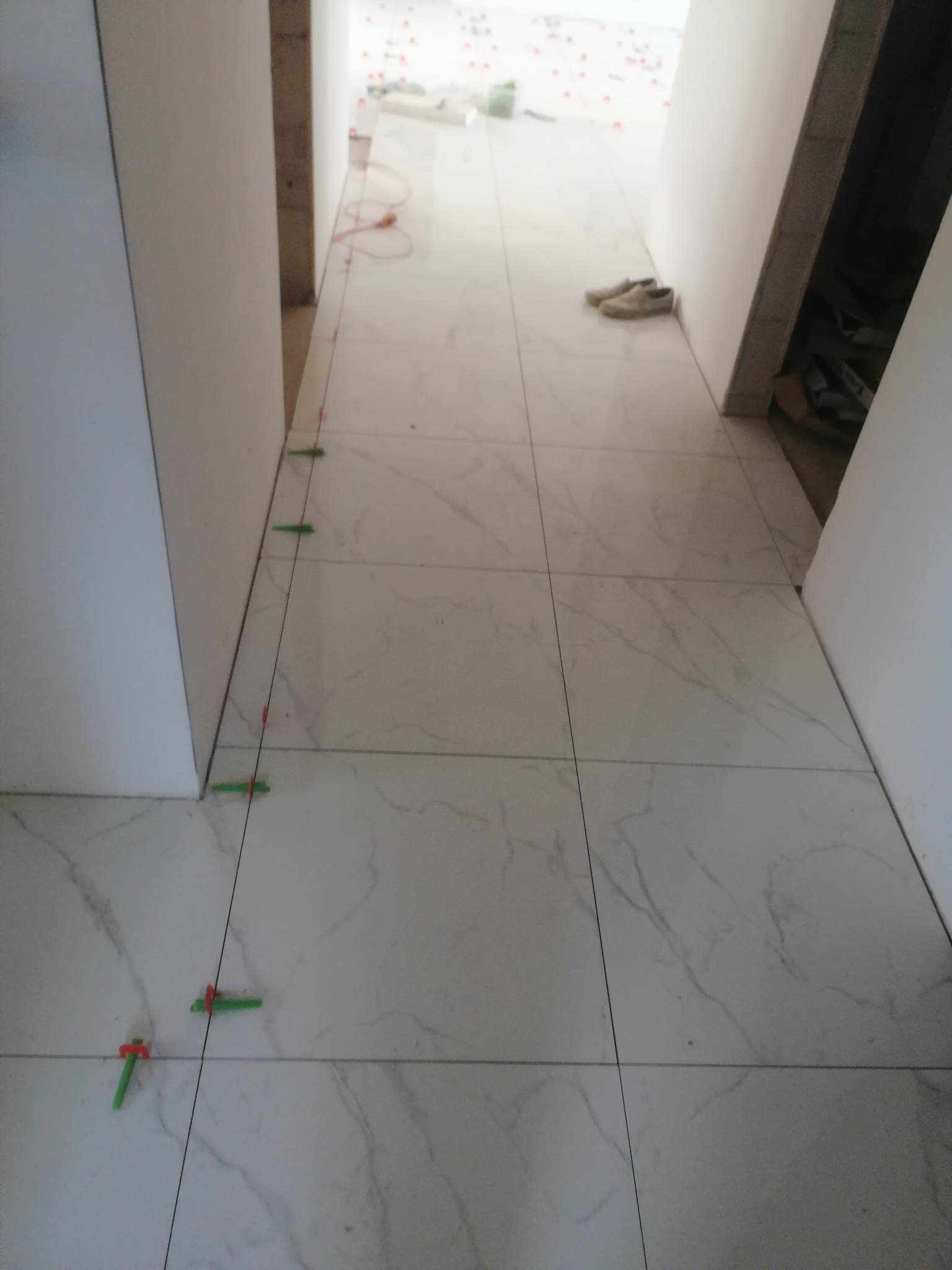 Układanie marmurowych płytek podłogowych w korytarzu z użyciem poziomicy i zielonych krzyżyków dystansowych.