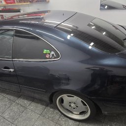 Kml_wyklejanki - Ciemny Mercedes CLK z przyciemnionymi szybami, widoczne naklejki na tylnej szybie. Auto stoi w garażu na szarej podłodze z płytek.