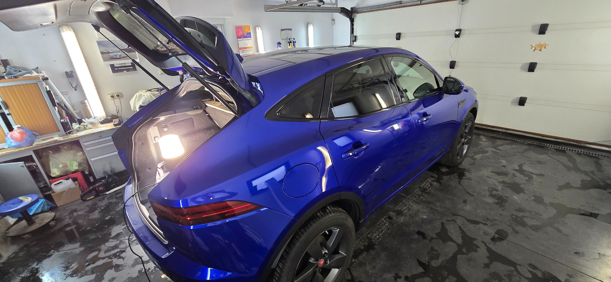 Błyszczący, niebieski Jaguar E-Pace po detailingu w Warszawie, z otwartą klapą bagażnika, widoczny w garażu z oświetleniem warsztatowym. Efekt hydrofobowy.
