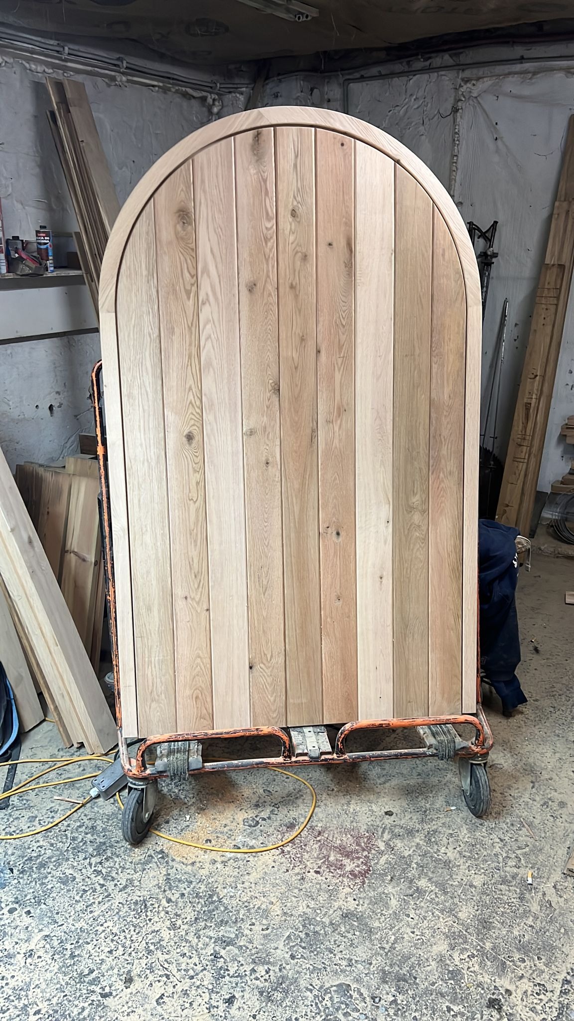 Duży, zaokrąglony panel z jasnego drewna na wózku transportowym w warsztacie, widoczne sęki i usłojenie drewna.