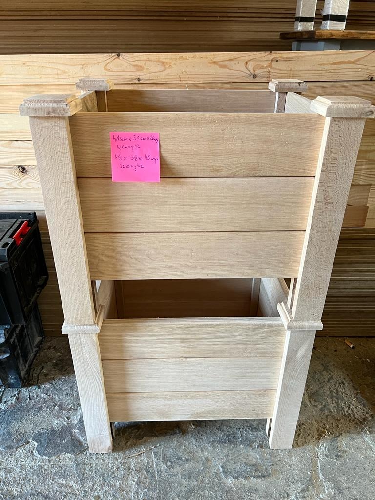 Surowa drewniana konstrukcja donicy na kwiaty z przyklejoną kartką z wymiarami, widok z przodu na podłodze w warsztacie.