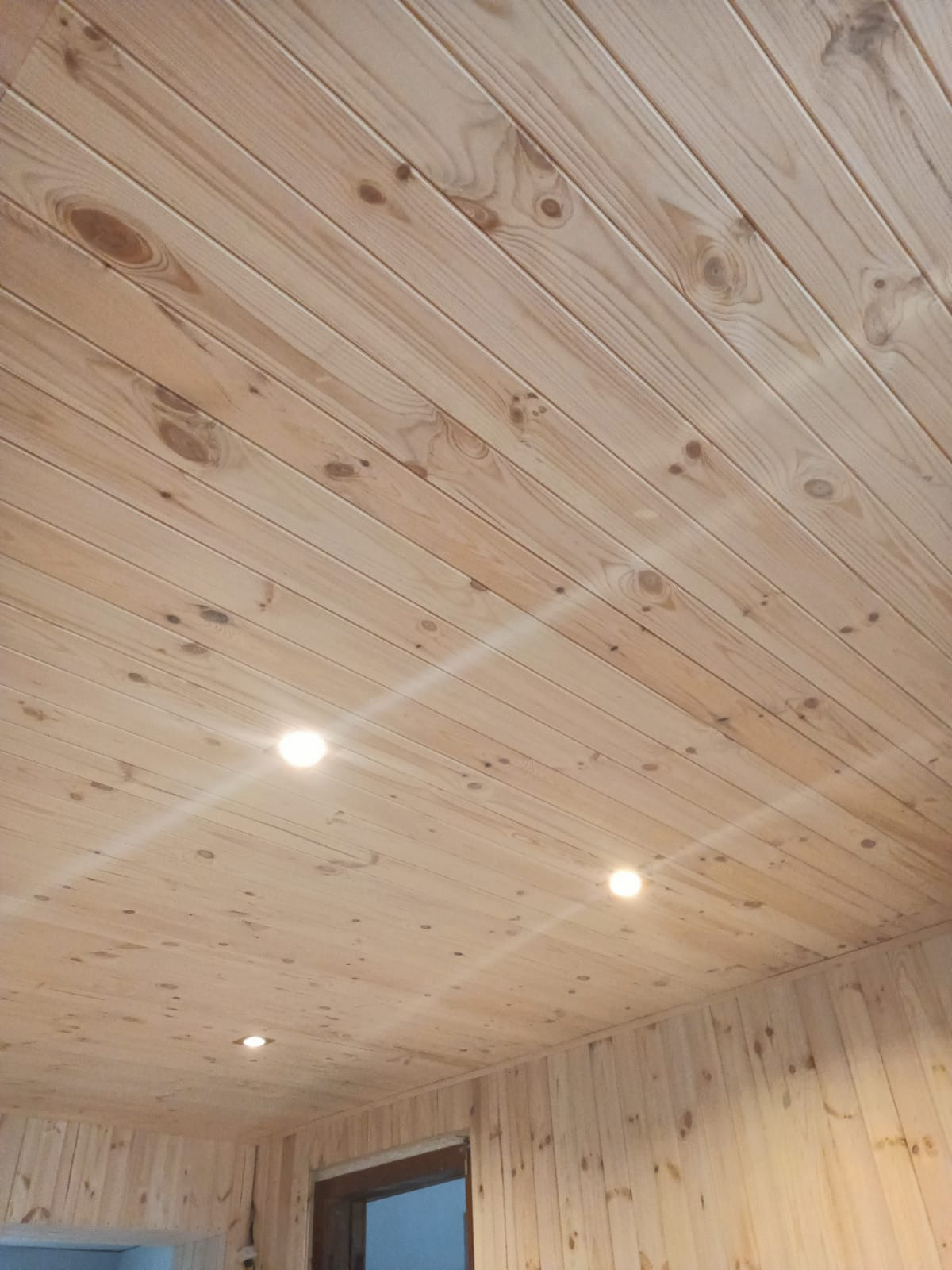 Drewniana boazeria na suficie i ścianach, oświetlenie punktowe, widoczny fragment drzwi.