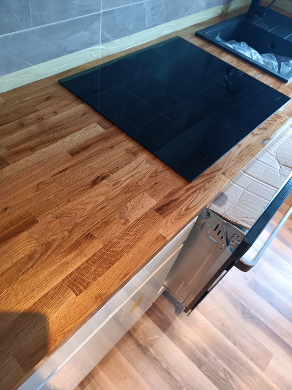 Montaż płyty indukcyjnej i zlewozmywaka w drewnianym blacie kuchennym, widoczne elementy montażowe piekarnika.