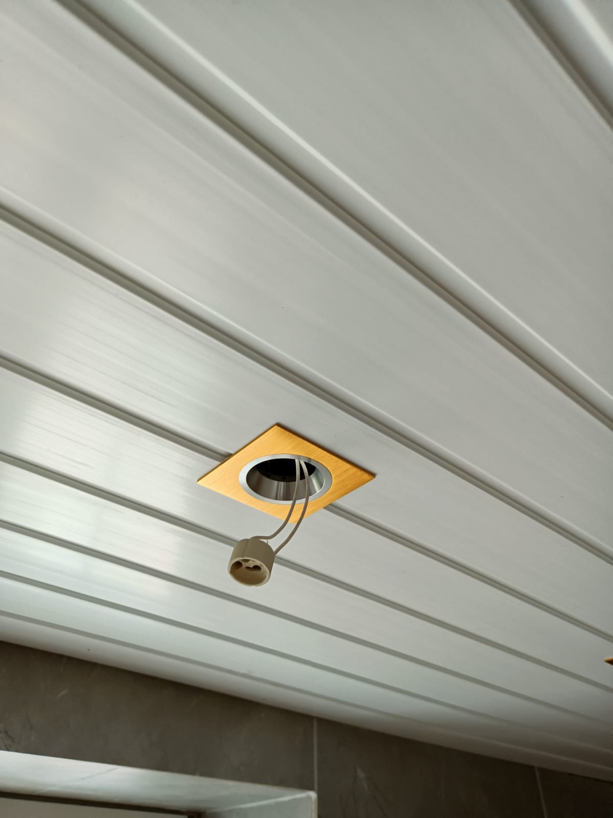 Panelowa biała podsufitka z wyciętym otworem na oświetlenie i wystającym kablem z oprawką żarówki.