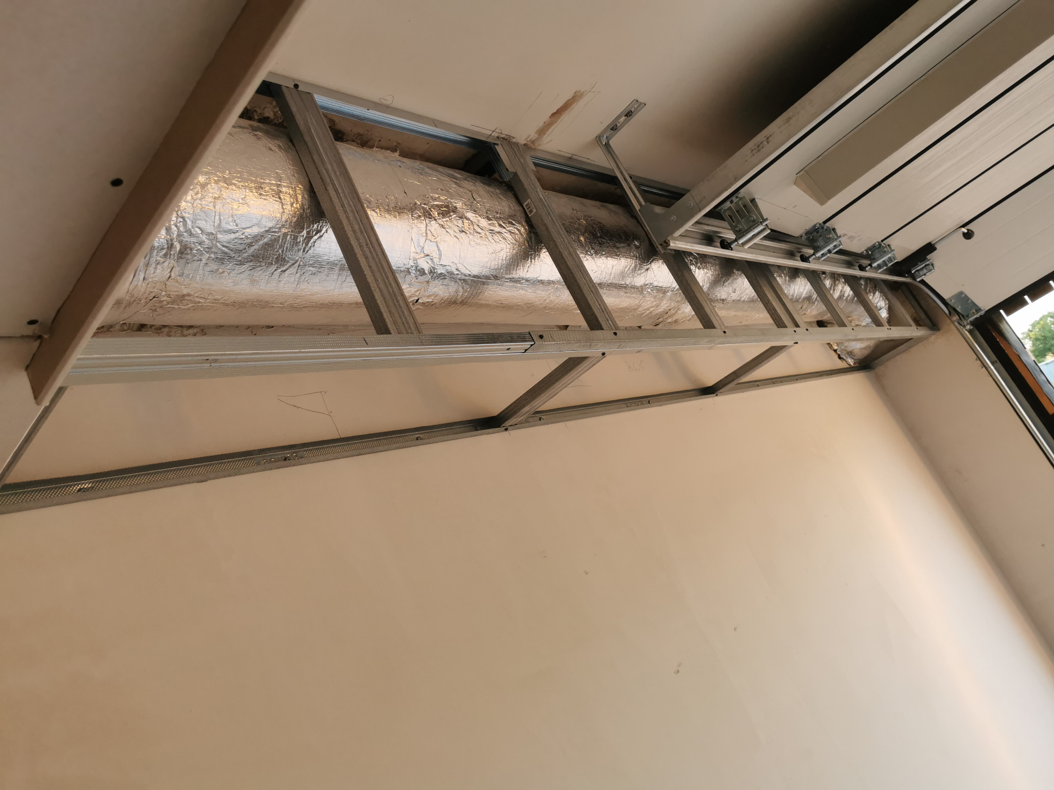 Montaż metalowej konstrukcji pod sufitem podwieszanym z widoczną izolacją termiczną, etap prac wykończeniowych.