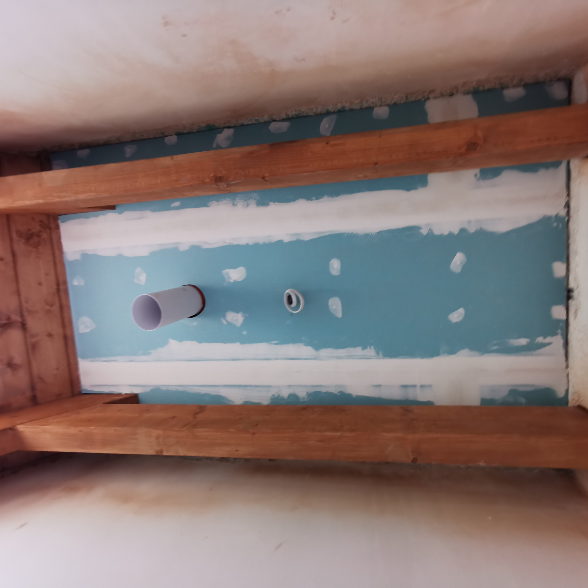 Widok z dołu na strop z drewnianymi belkami, płytą kartonowo-gipsową pomalowaną na niebiesko z widocznymi punktami szpachlowania oraz wystającą rurą wentylacyjną i instalacją elektryczną.