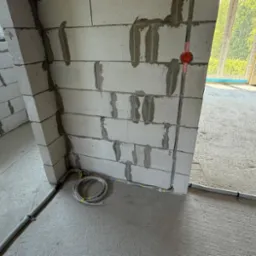 Surowy stan: przewody elektryczne w ścianach z betonu komórkowego, okrągła puszka instalacyjna, przewody ułożone na podłodze. W tle okno i surowe ściany.