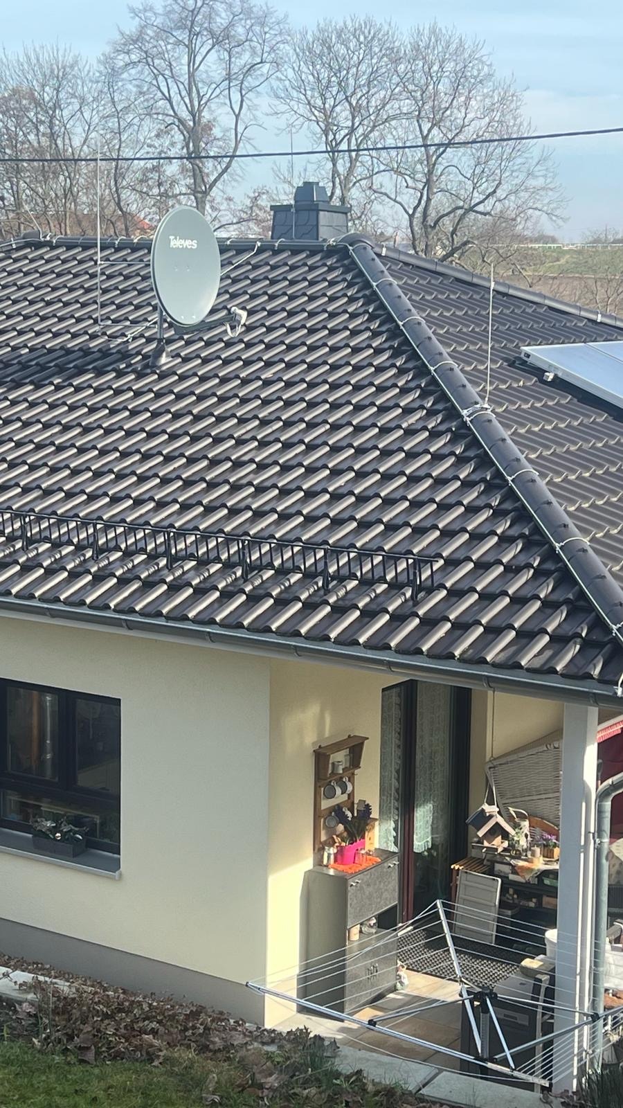 Dom jednorodzinny z brązowym dachem pokrytym dachówką, na którym zamontowana jest antena satelitarna Televes oraz instalacja odgromowa z widocznymi przewodami i odgromnikami. Na dachu widoczny...