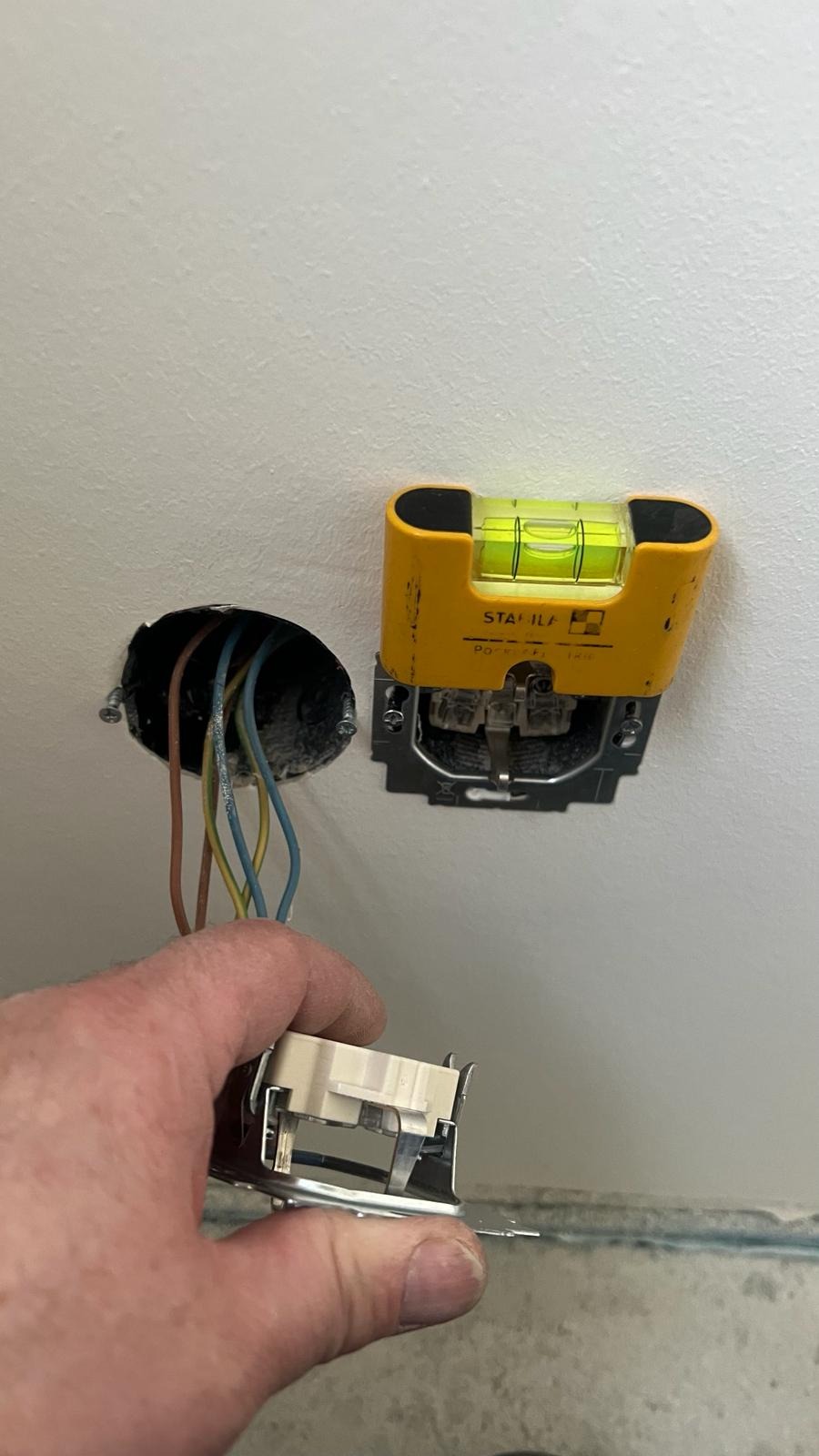 Elektryk montuje gniazdko elektryczne w ścianie, używając poziomicy Stabila do precyzyjnego ustawienia.