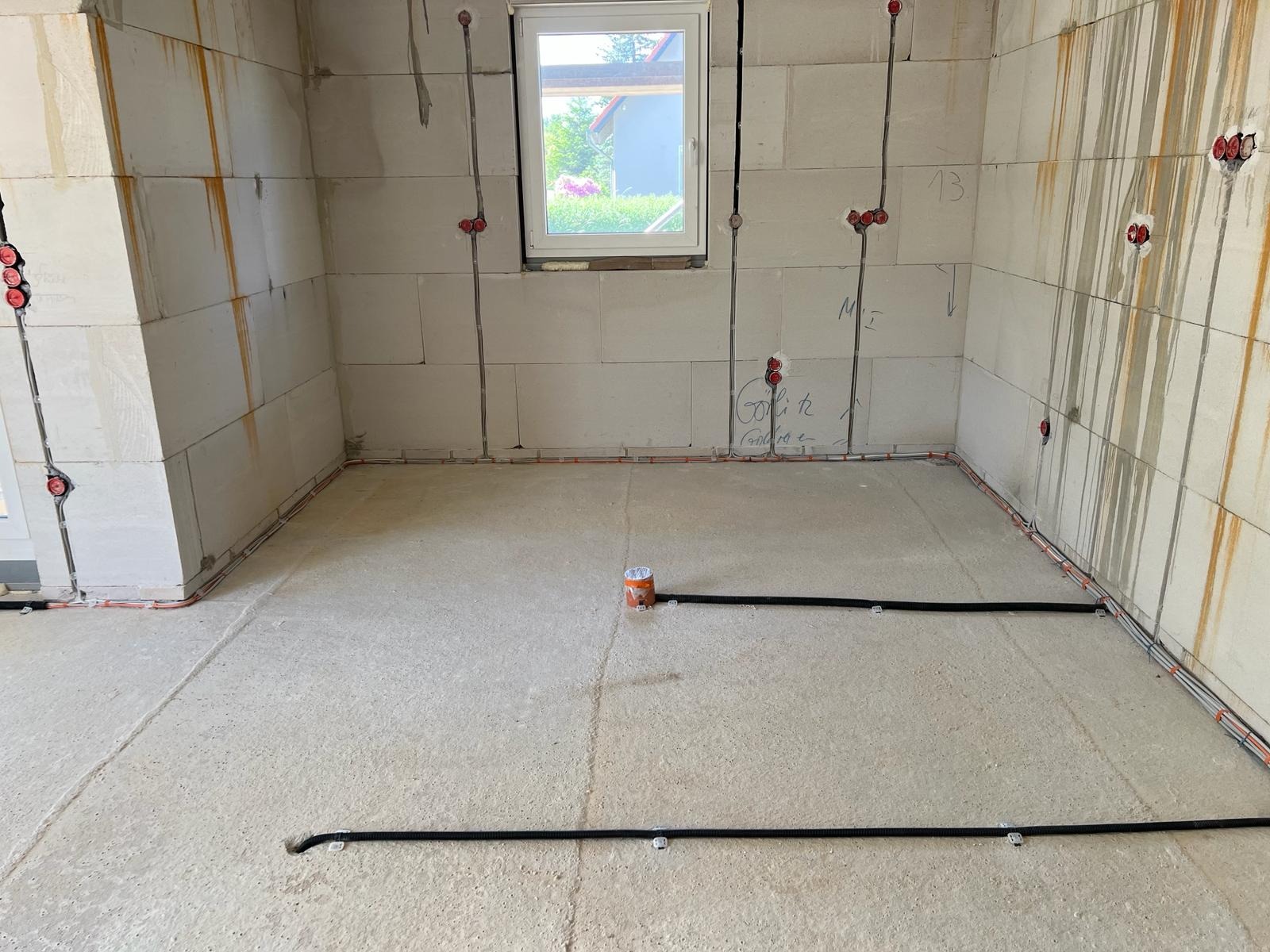 Surowy stan wnętrza z widocznymi przewodami elektrycznymi w ścianach z betonu komórkowego i peszlami na podłodze, przygotowane do dalszych prac wykończeniowych.
