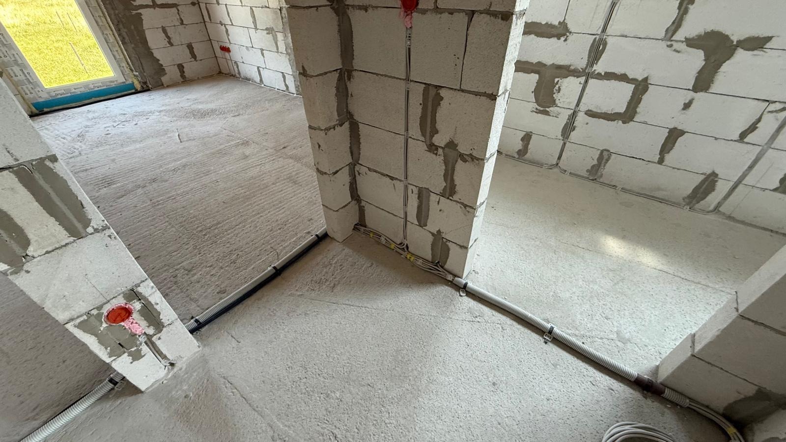 Wnętrze w stanie surowym z widoczną instalacją elektryczną w peszlach i puszkami w ścianach z betonu komórkowego, przygotowane do dalszych prac wykończeniowych.